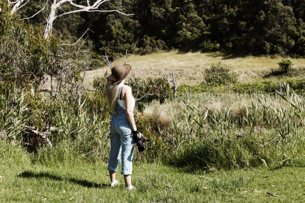 A woman holding a camera looking towards a forest and open field