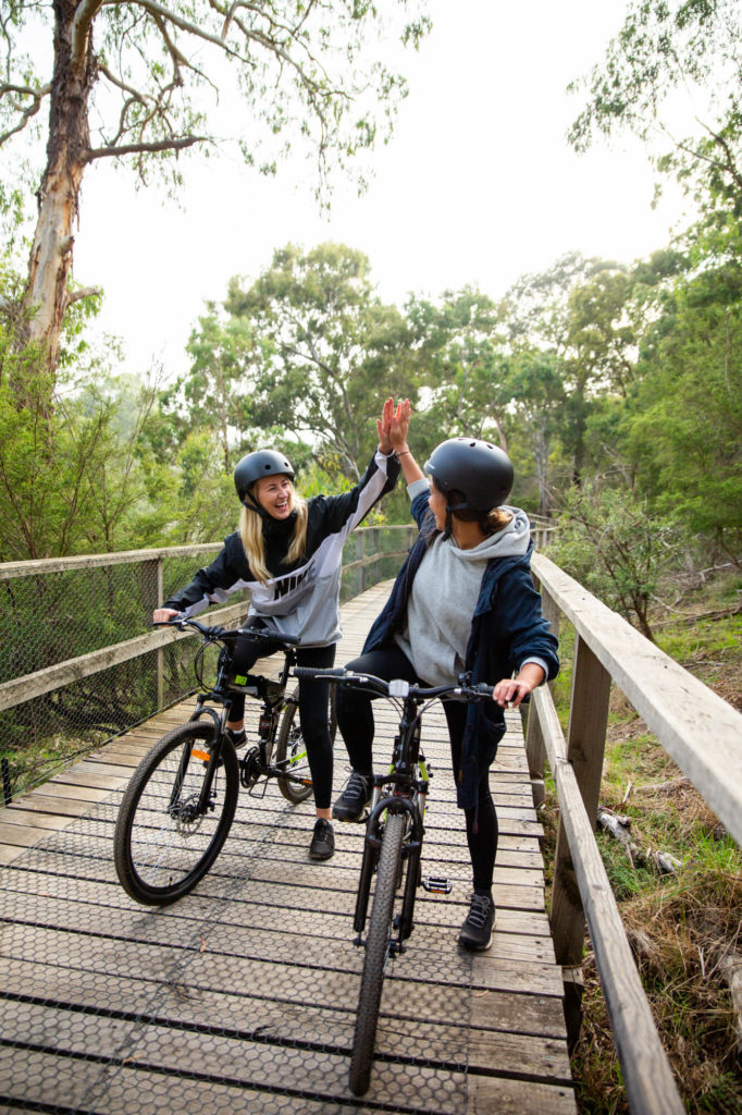 Two people high-fiving on bikes on a path surrounded by nature
