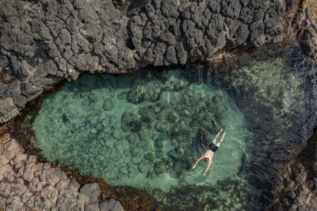 Overhead view of man swimming in large natural rock with crystal clear water