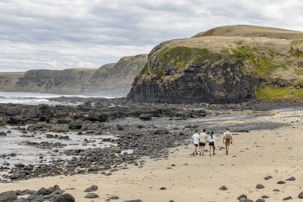 Adventure Tour Guide walks with small group on secluded ocean beach with clifftops in the distance